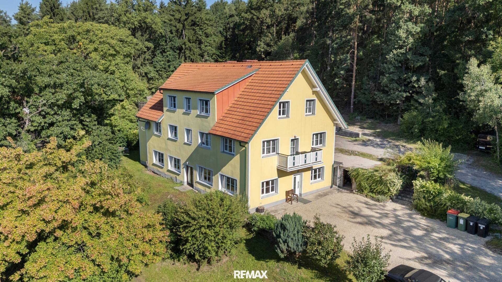 Vogelperspektive des gelben Hauses mit rotem Dach, umgeben von Bäumen und einer großen Auffahrt.