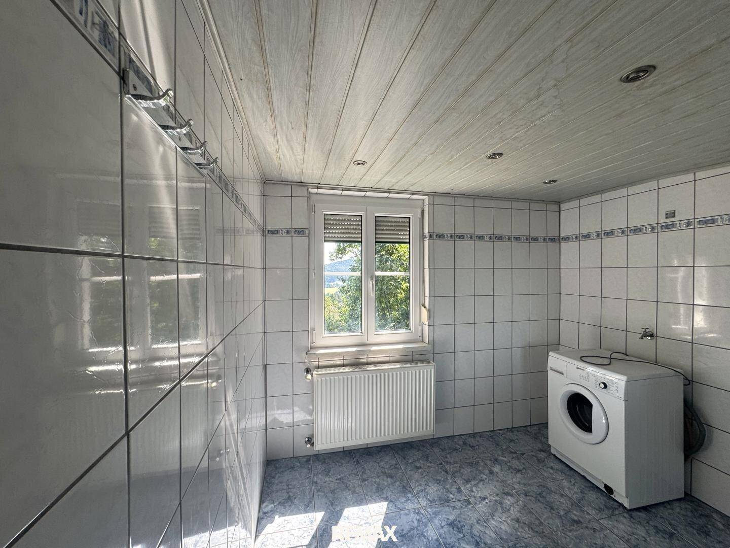 Waschküche mit Fliesen an Wänden und Boden, Fenster und Waschmaschine.