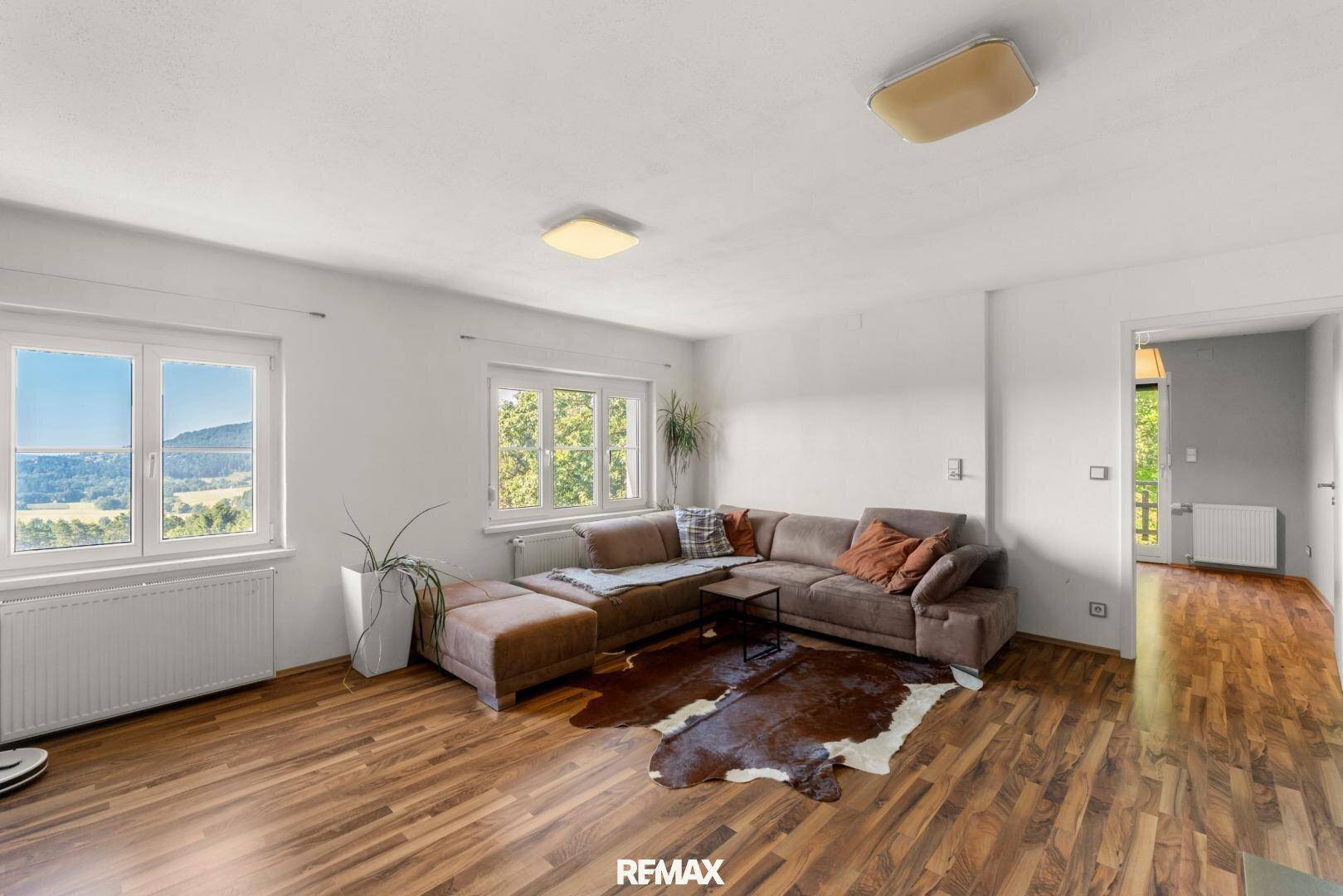 Gemütliches Wohnzimmer mit großem Sofa, Holzboden und weitem Blick ins Grüne.