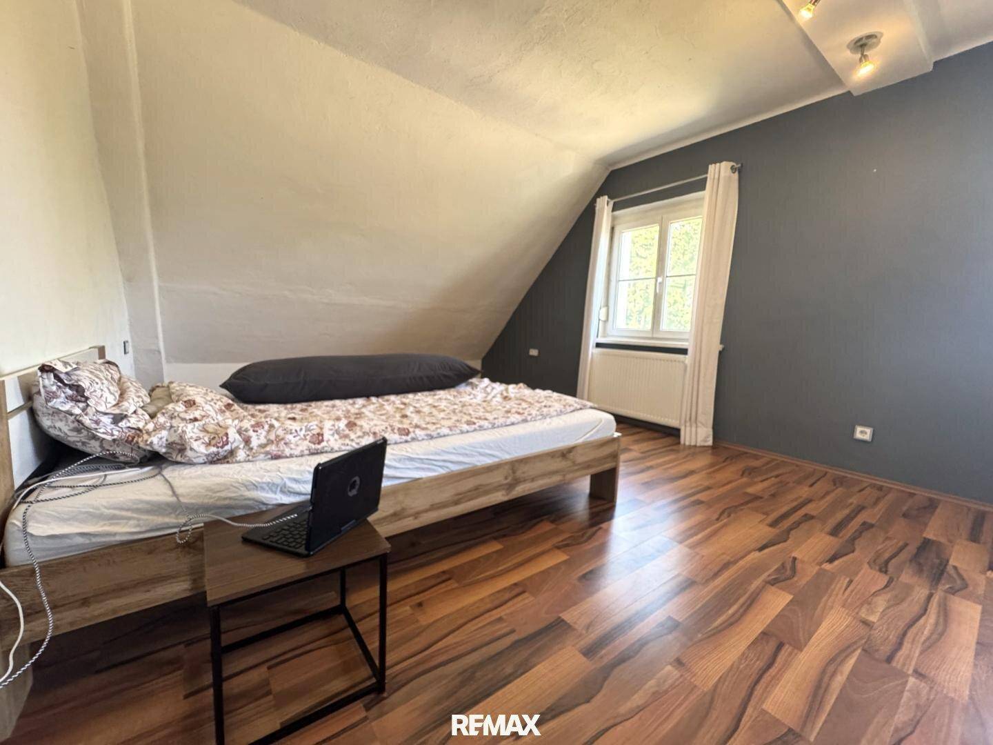 Schlafzimmer mit Holzboden, Bett und einem Fenster unter der Dachschräge.