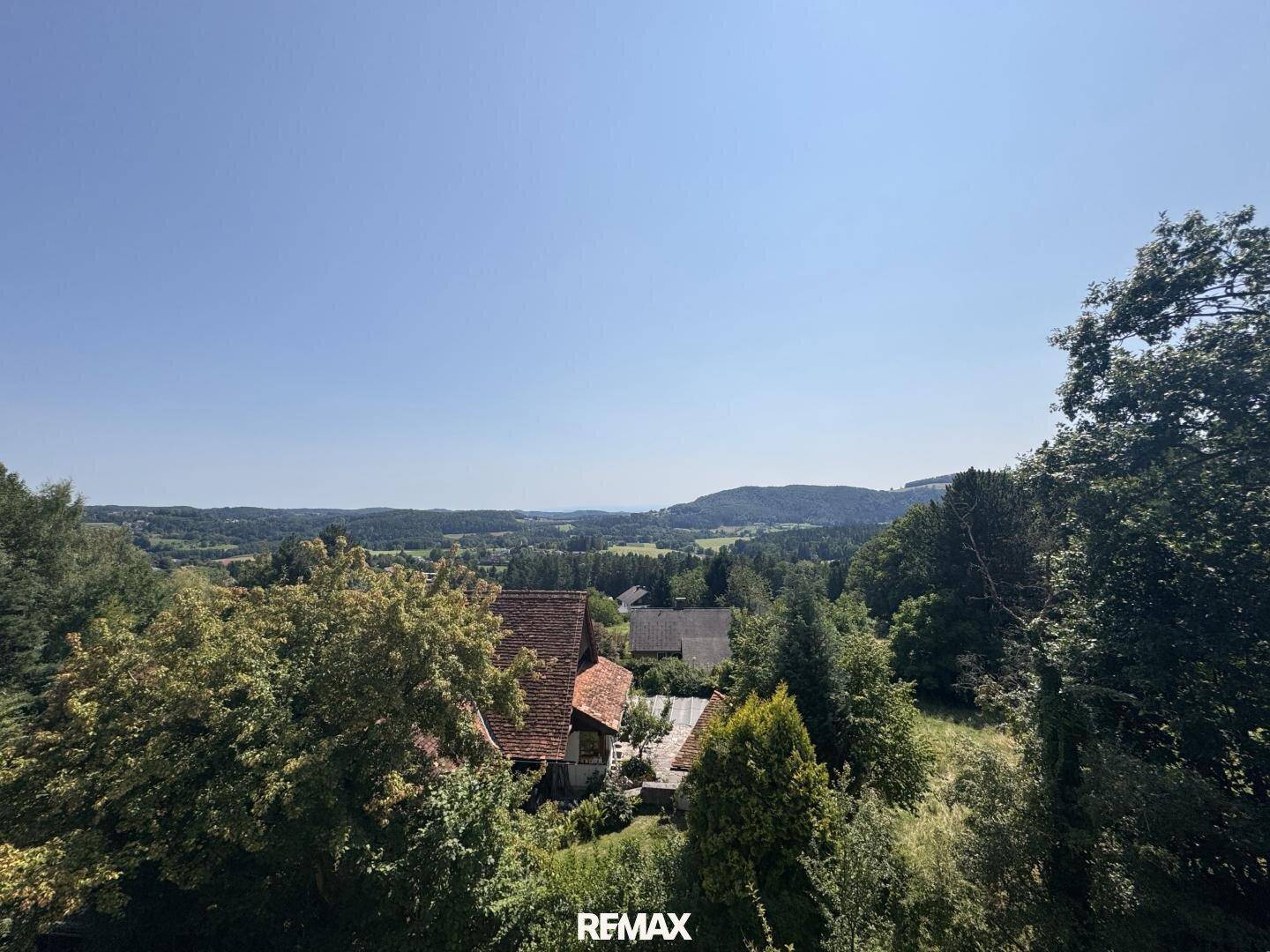 Weitläufiger Panoramablick über die grüne Landschaft mit Hügeln und Wäldern unter blauem Himmel.
