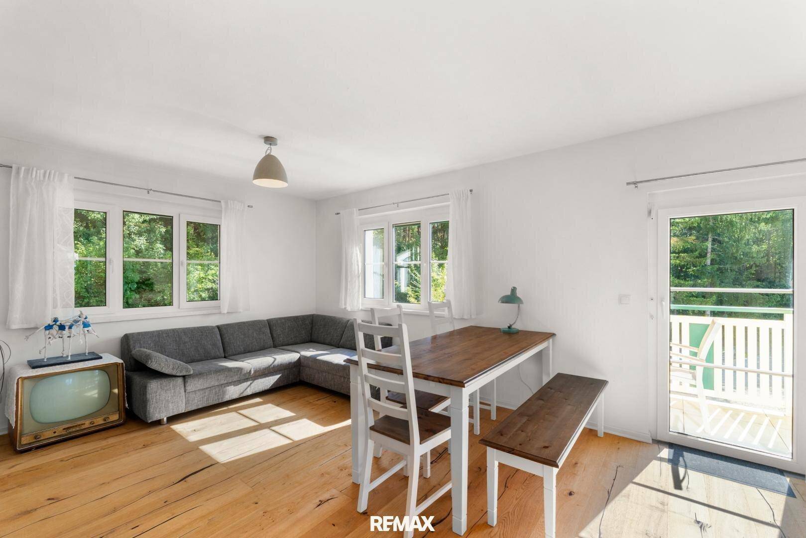 Heller Ess- und Wohnbereich mit Holztisch, Sofa und direktem Zugang zum Balkon oder zur Terrasse.