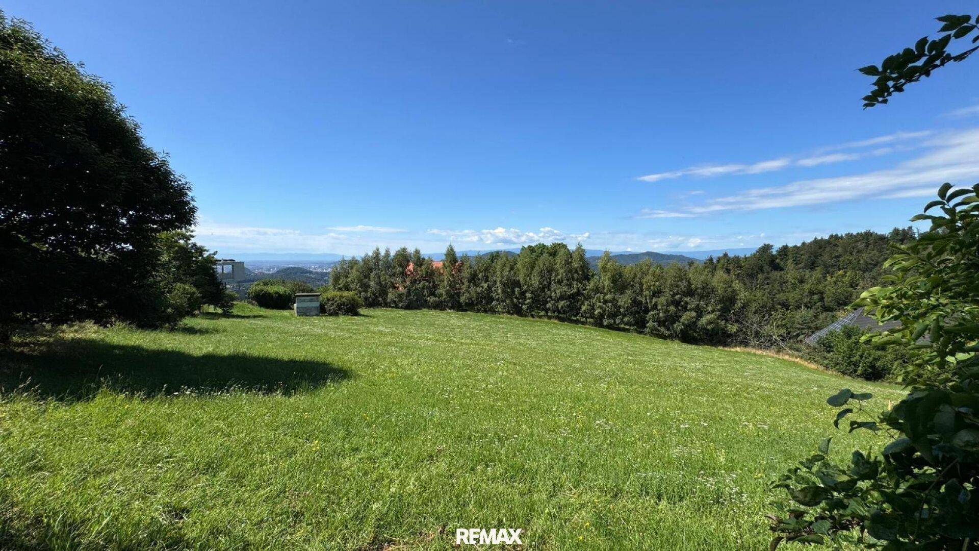 Ausgedehnte grüne Fläche mit Blick auf die hügelige Landschaft und eine Siedlung in der Ferne.