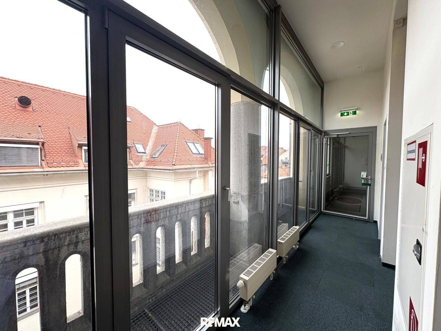 Heller Flur mit großen Fenstern, die auf einen Balkon blicken, und einem Ausgangsschild über der Tür.