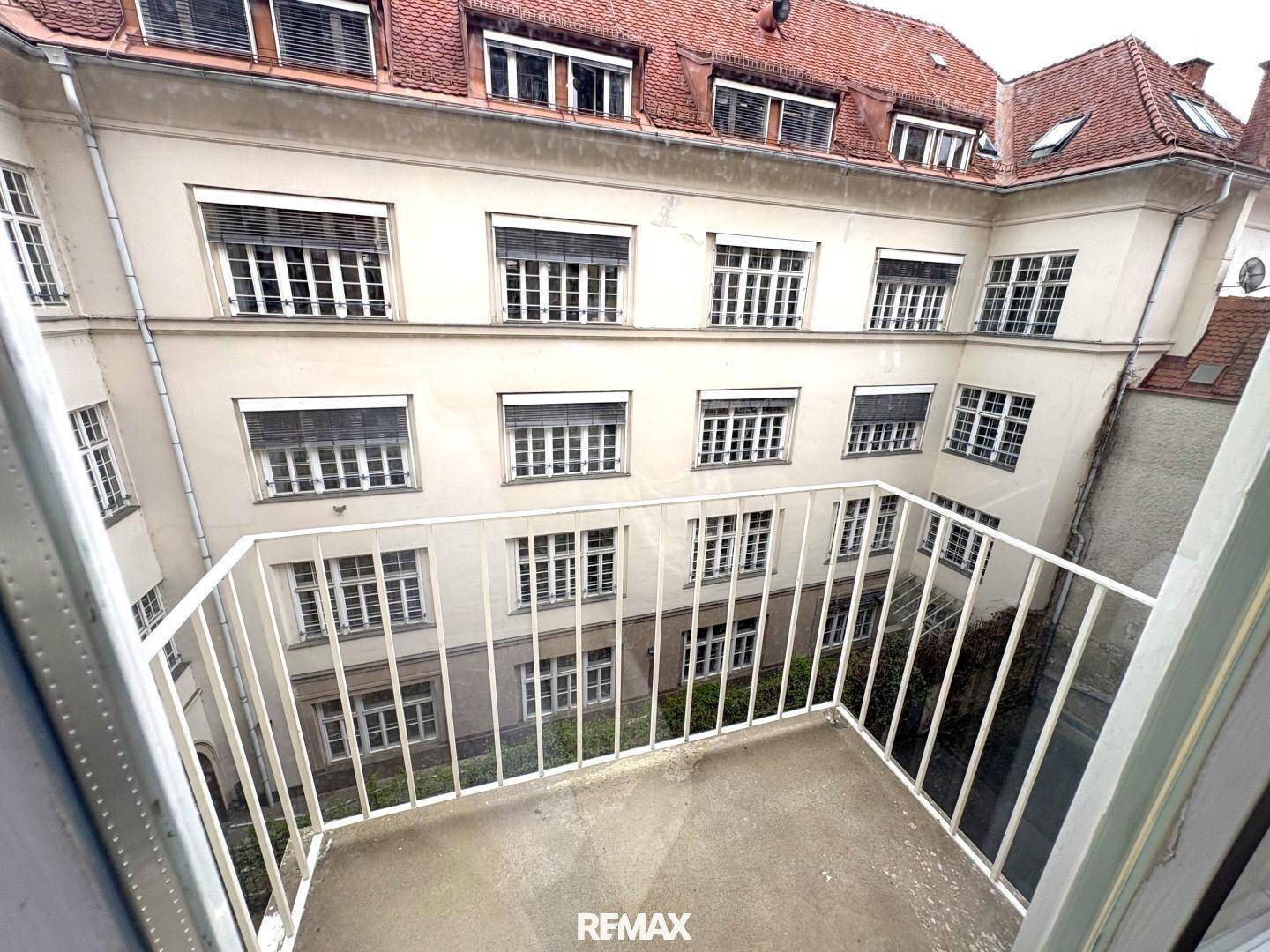 Kleiner Balkon mit Blick auf einen ruhigen Innenhof mit vielen Fenstern und traditioneller Architektur.