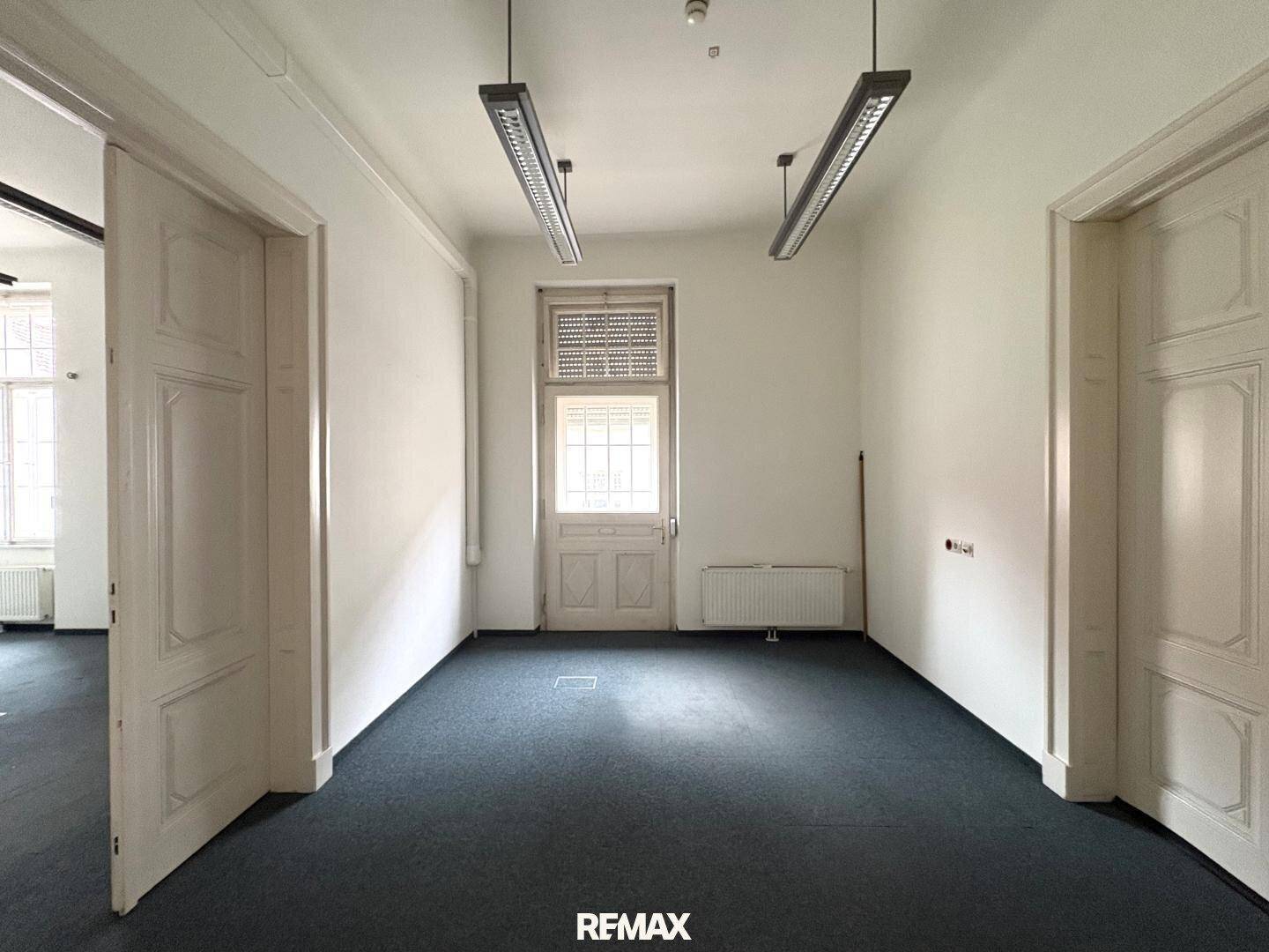 Heller Büroraum mit dunklem Teppichboden, weißen Wänden und einer traditionellen Tür mit Fenster.
