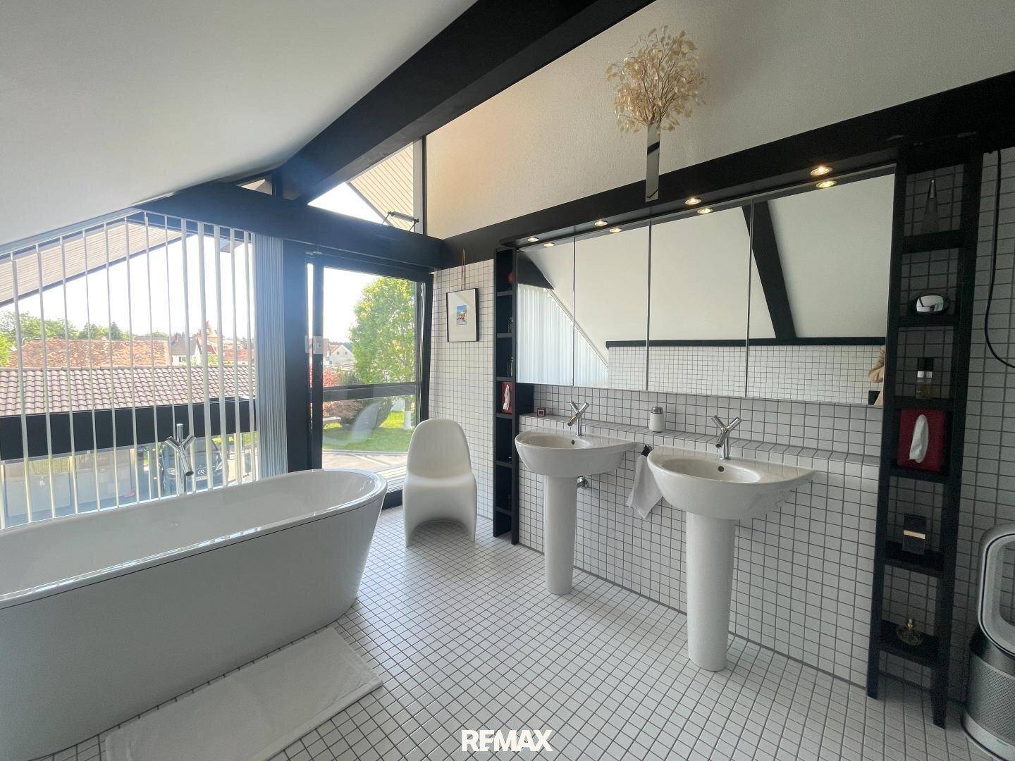 Geräumiges Badezimmer mit freistehender Badewanne, zwei Waschbecken und großem Spiegel.