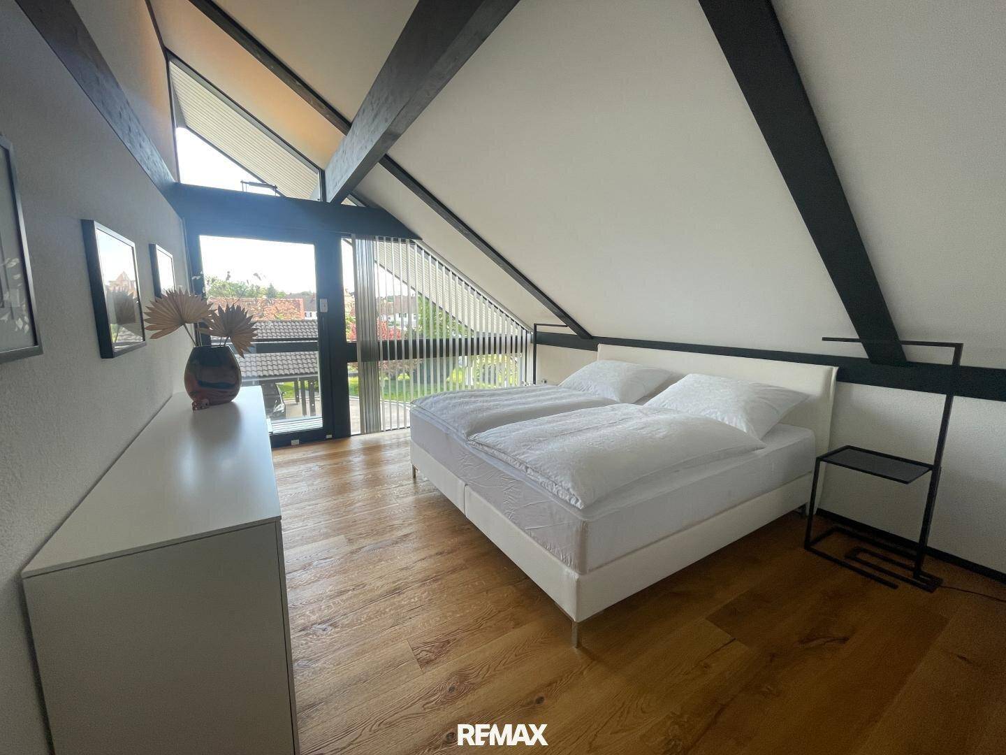 Schlafzimmer im Dachgeschoss mit Holzboden, Doppelbett und Zugang zu einem Balkon mit Aussicht.