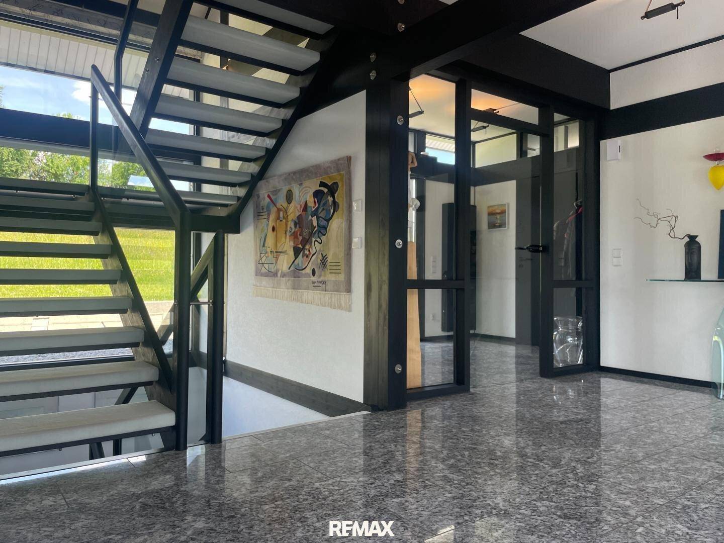 Heller Eingangsbereich mit moderner Treppe, glänzendem Steinboden und Kunst an der Wand.