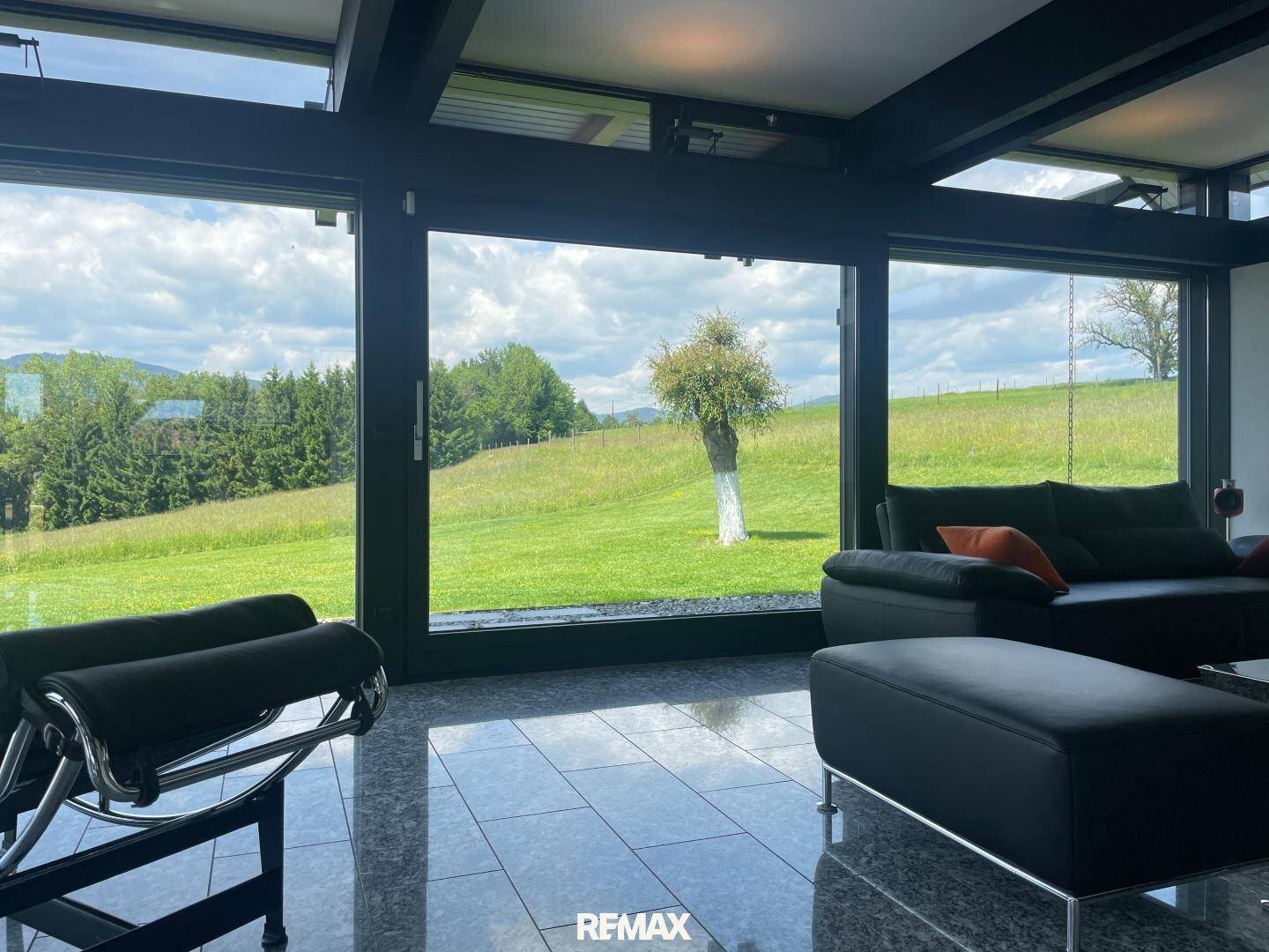 Helles Wohnzimmer mit bequemen Ledersofas, Steinboden und Panoramafenstern mit weitem Grünblick.