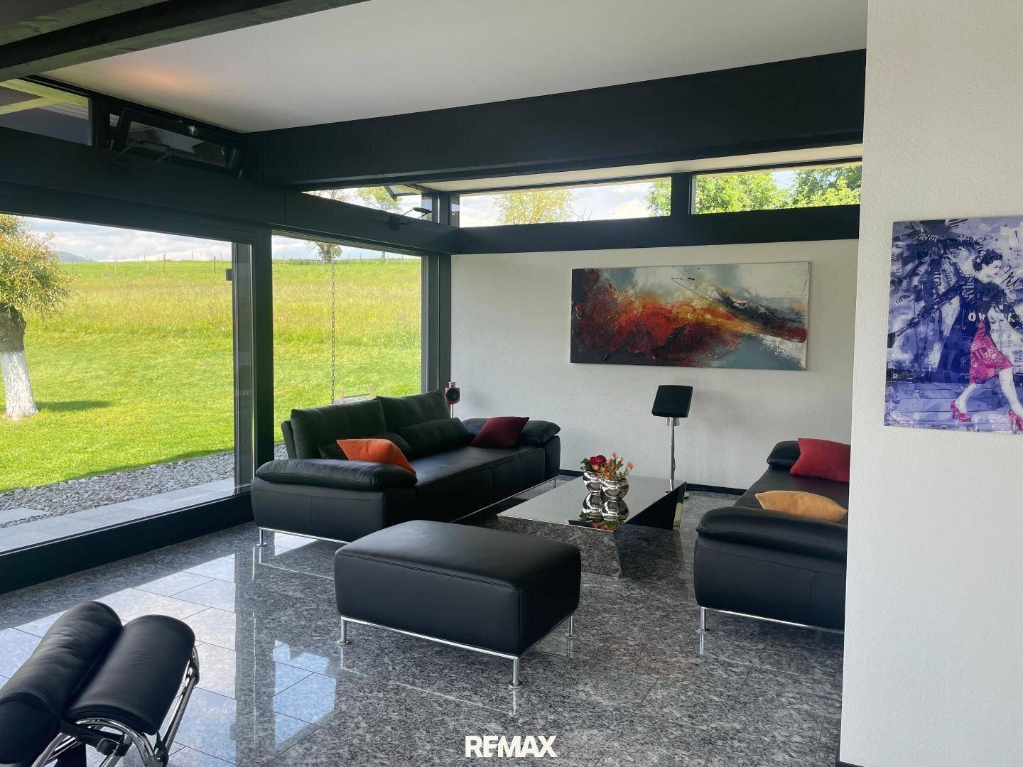 Geräumiges Wohnzimmer mit moderner Einrichtung, Kunst an der Wand und großen Fenstern mit Blick ins Grüne.