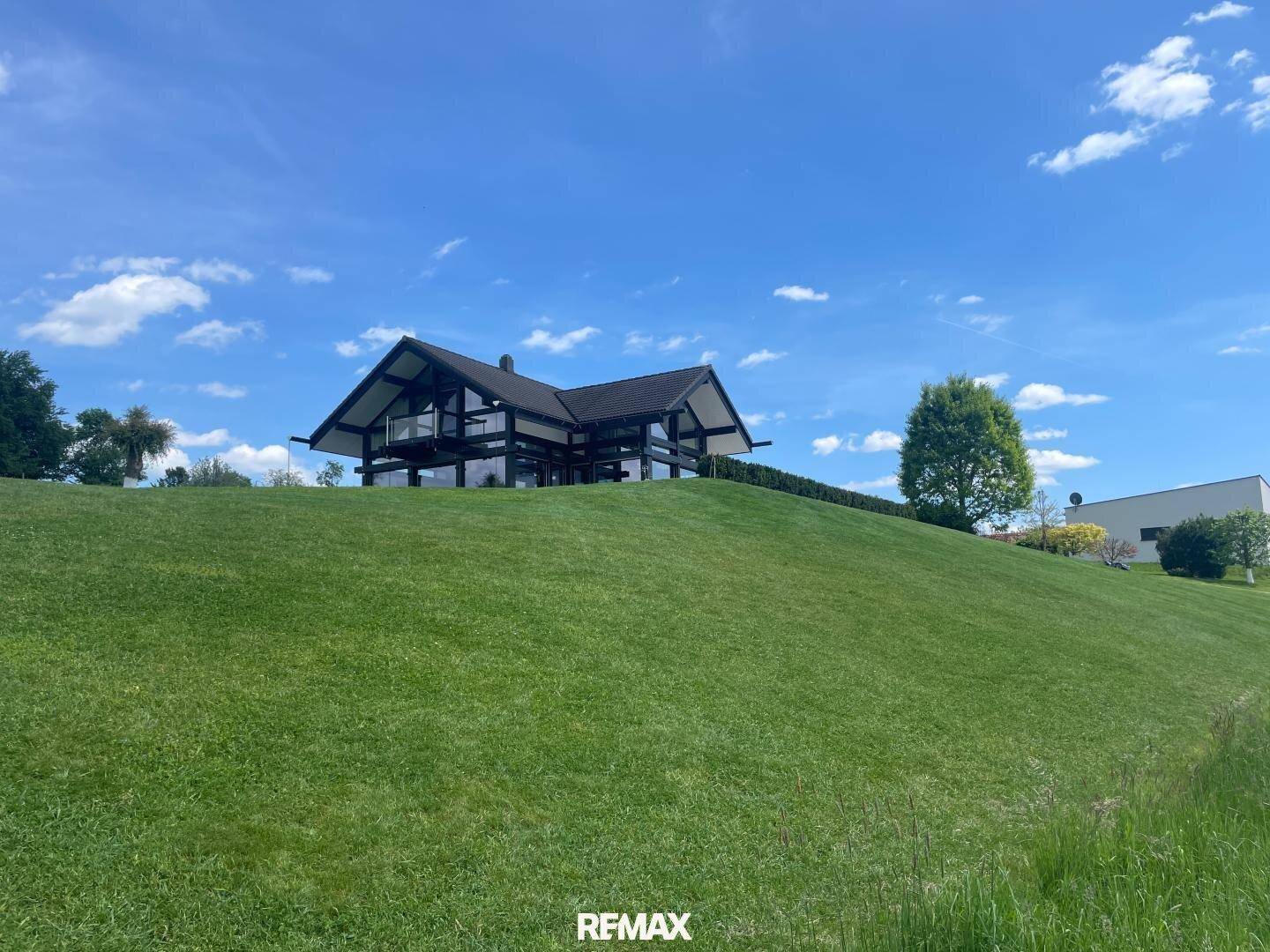 Das moderne Haus thront auf einem grünen Hügel und bietet einen weiten Blick über die umliegende Landschaft.