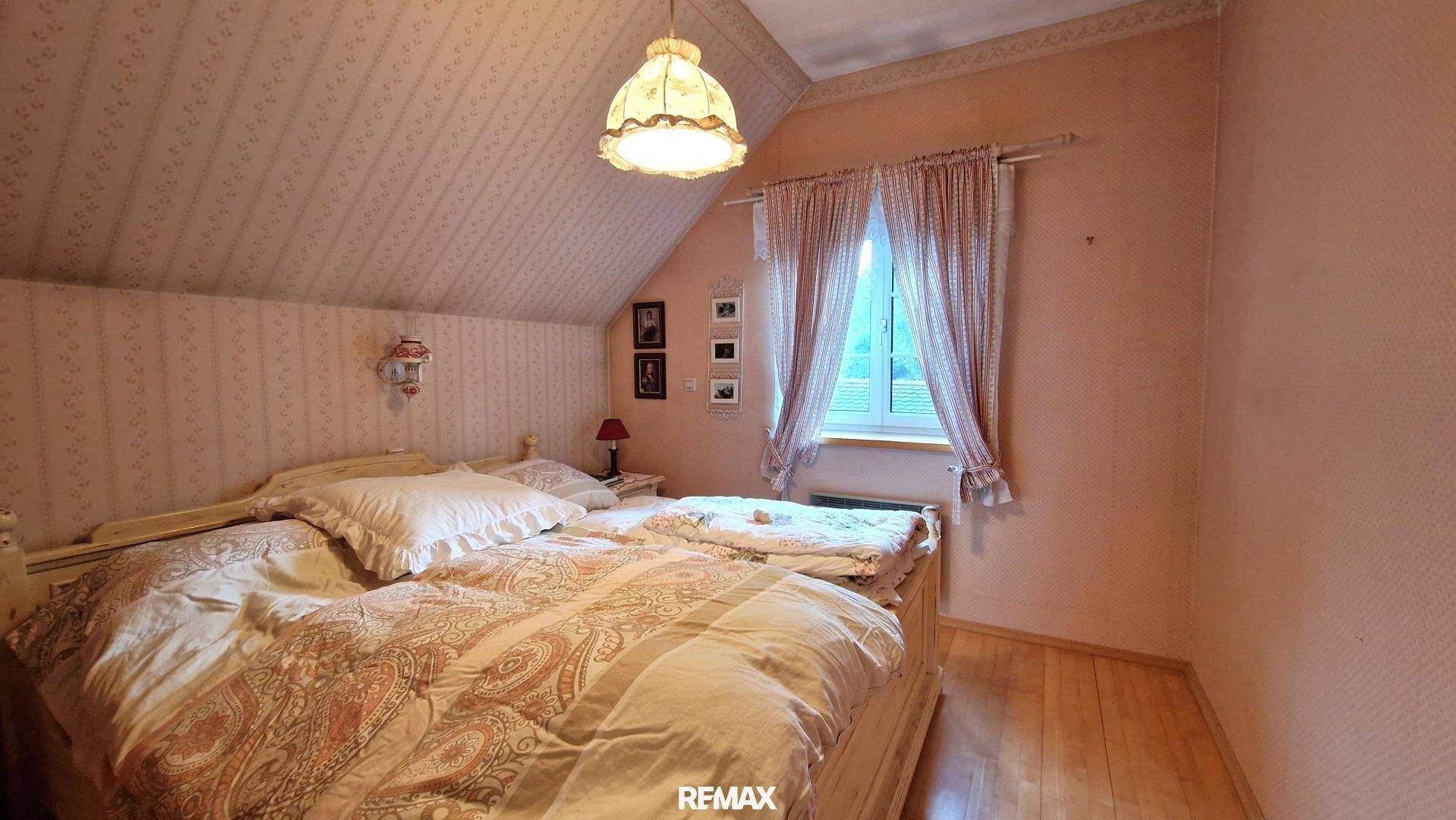 Gemütliches Schlafzimmer im Dachgeschoss mit Doppelbett, Holzfußboden und gemusterter Tapete.