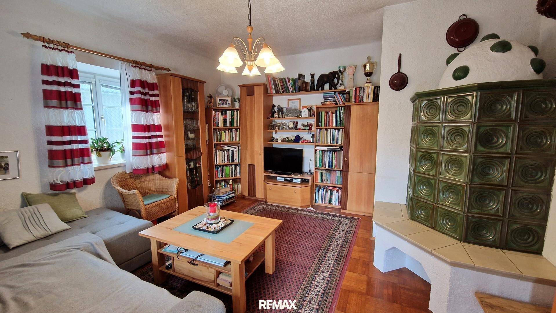 Wohnzimmer mit Kachelofen, Parkettboden und Bücherregalen, die eine gemütliche Atmosphäre schaffen.