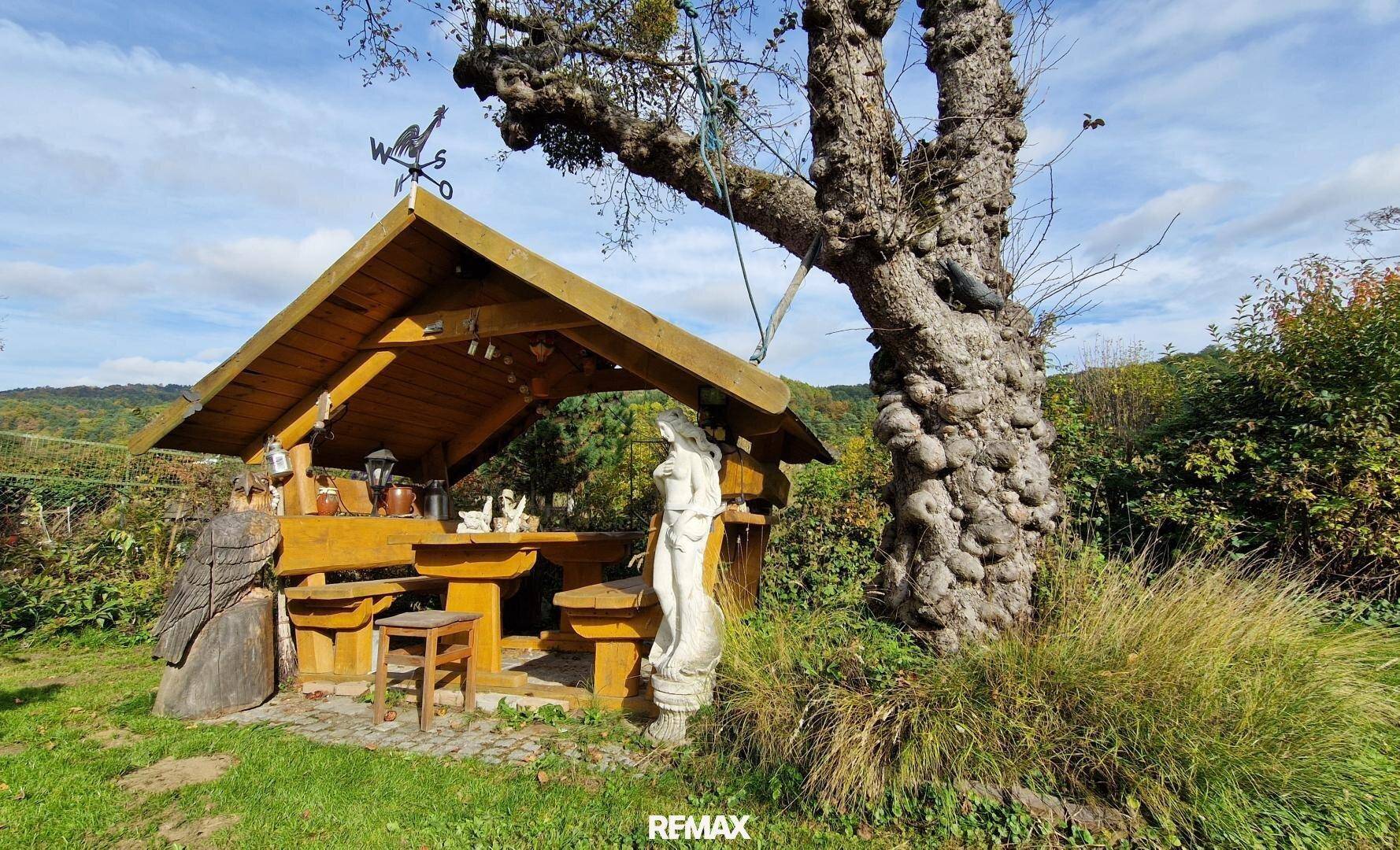 Detailansicht des rustikalen Holzpavillons mit Sitzgelegenheiten und Dekorationen im Garten.