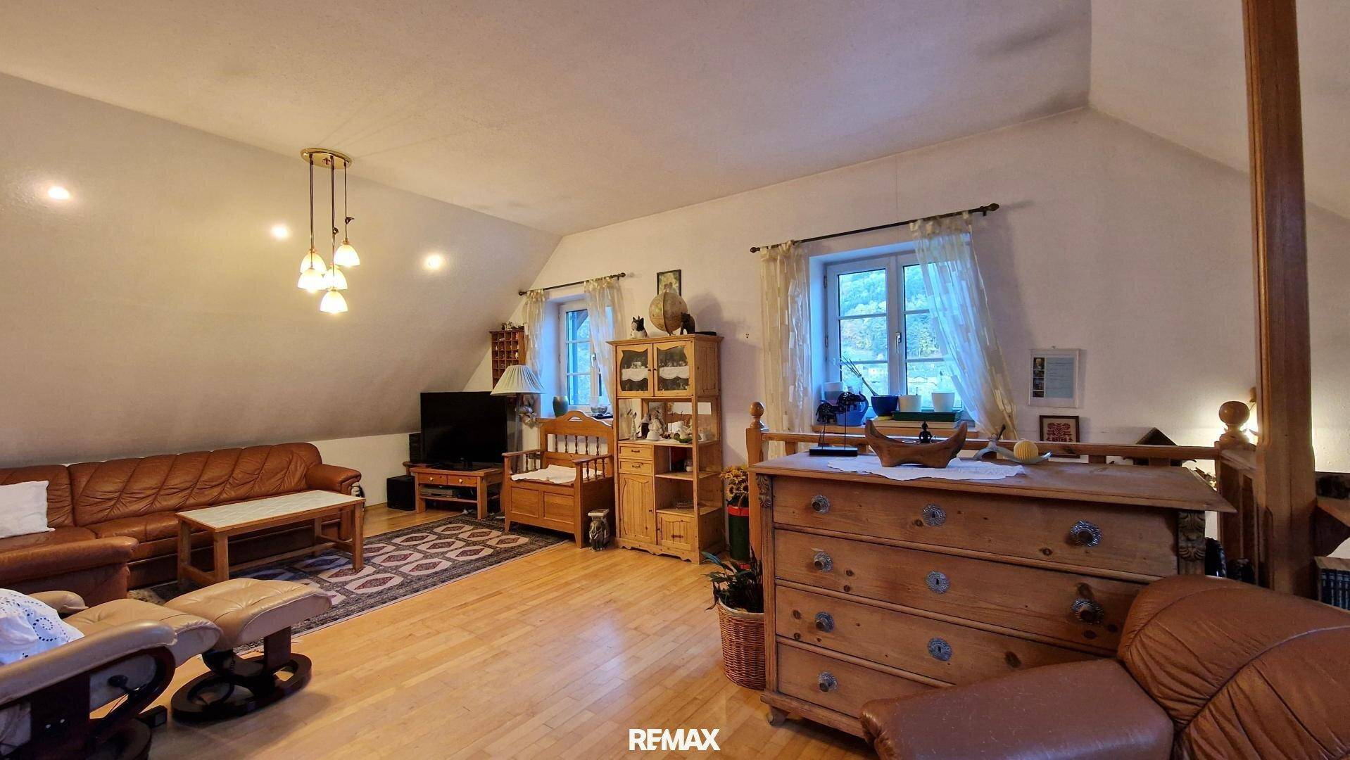 Helles Dachgeschoss-Wohnzimmer mit bequemen Möbeln und Blick aus den Fenstern.