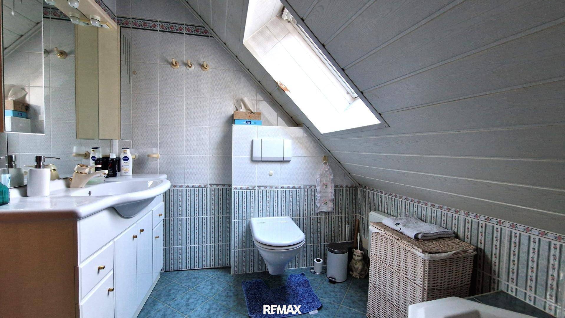 Badezimmer im Dachgeschoss mit Dachfenster, WC und Waschtisch, gefliest in Blau- und Weißtönen.