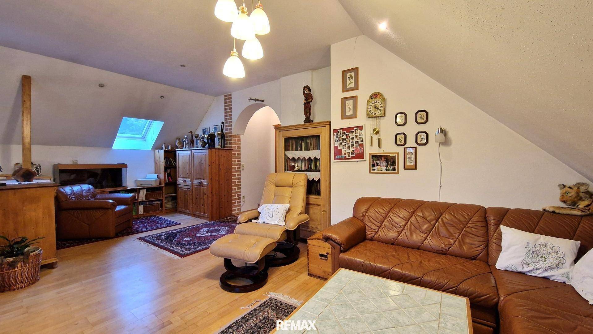Geräumiges Wohnzimmer im Dachgeschoss mit Ledersofa, Holzboden und Dachfenster.