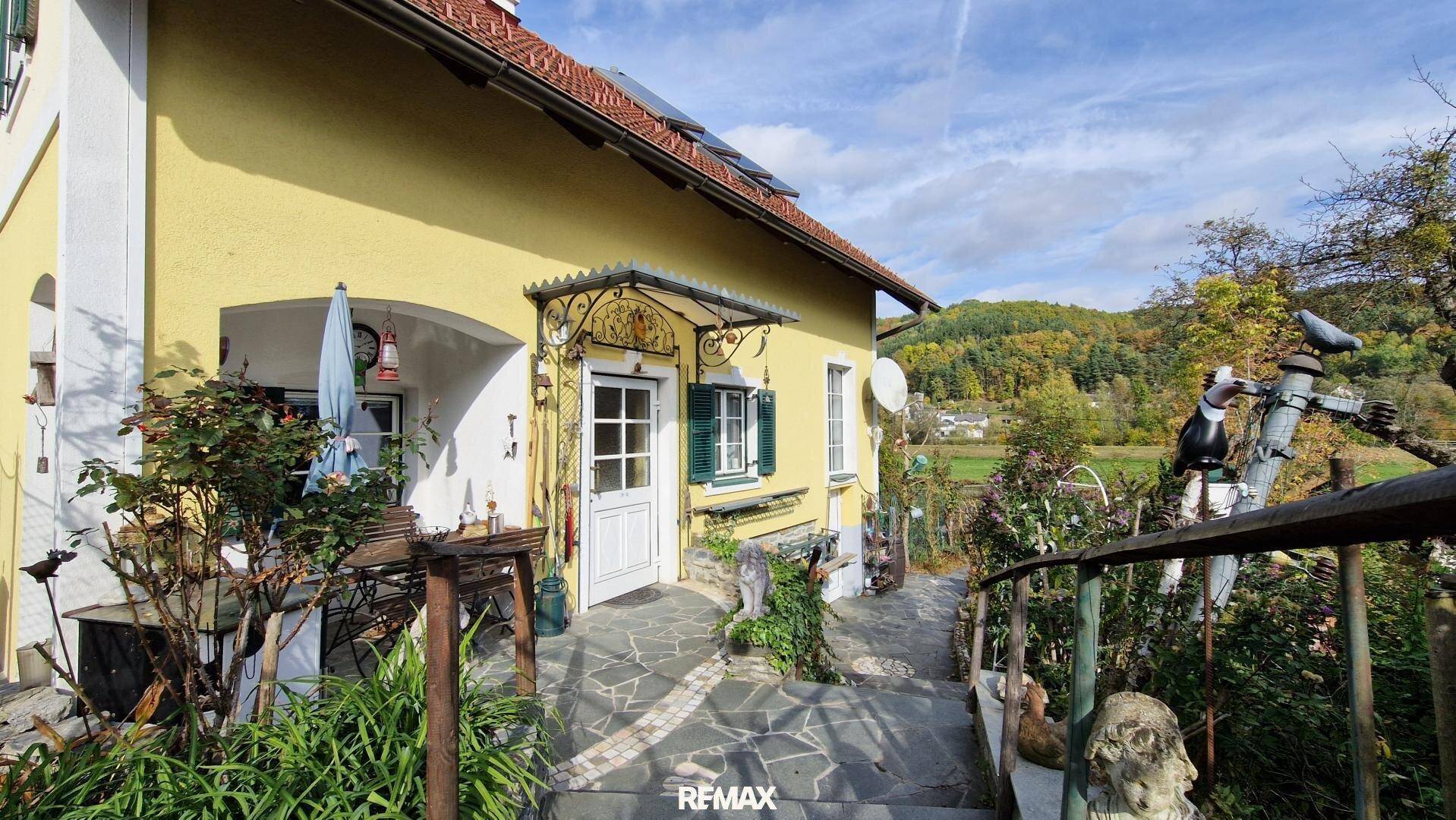 Eingangsbereich des Hauses mit Steinfliesen, einem Vordach und Blick auf die grüne Landschaft.