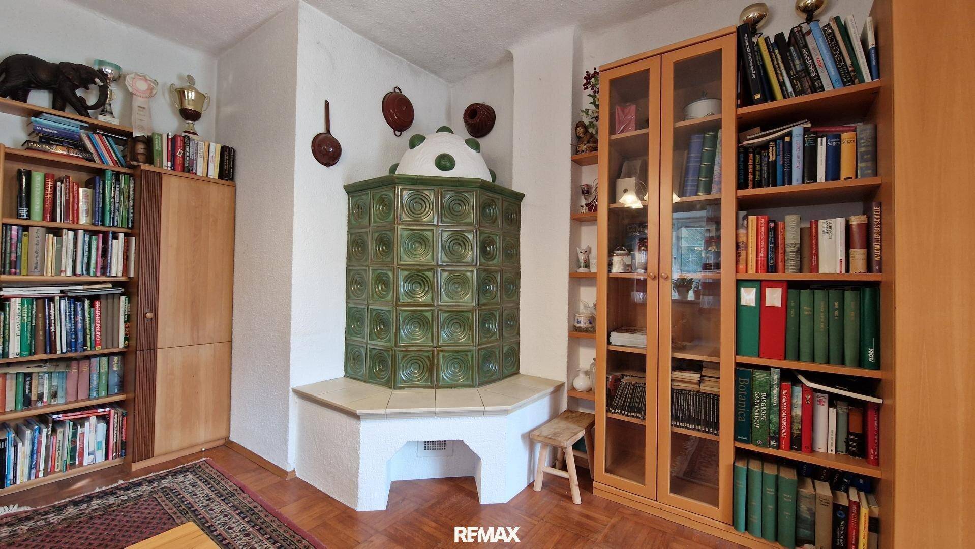 Grüner Kachelofen als zentrales Element im Wohnzimmer, umgeben von Bücherregalen.