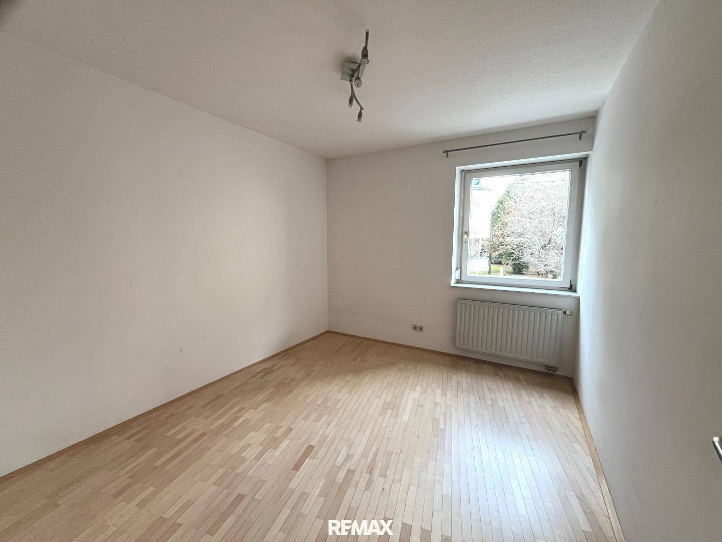 Helles, unmöbliertes Schlafzimmer mit Parkettboden, weißen Wänden und einem Fenster mit Ausblick.