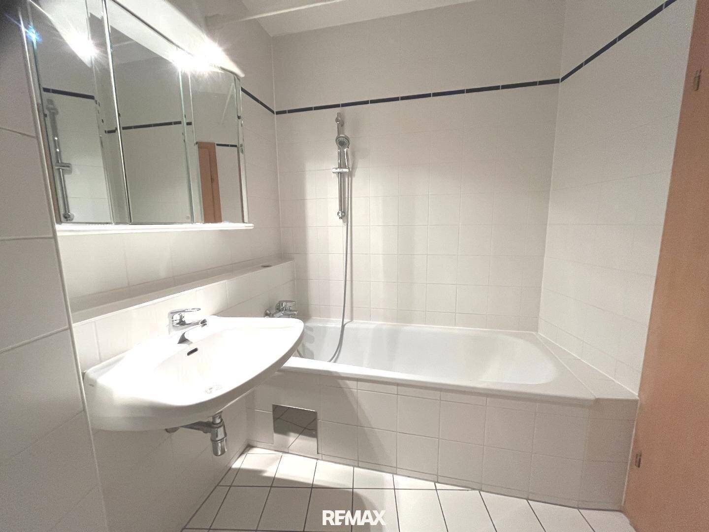 Badezimmer mit weiß gefliester Badewanne, Duschfunktion und einem Waschbecken mit Spiegelschrank.