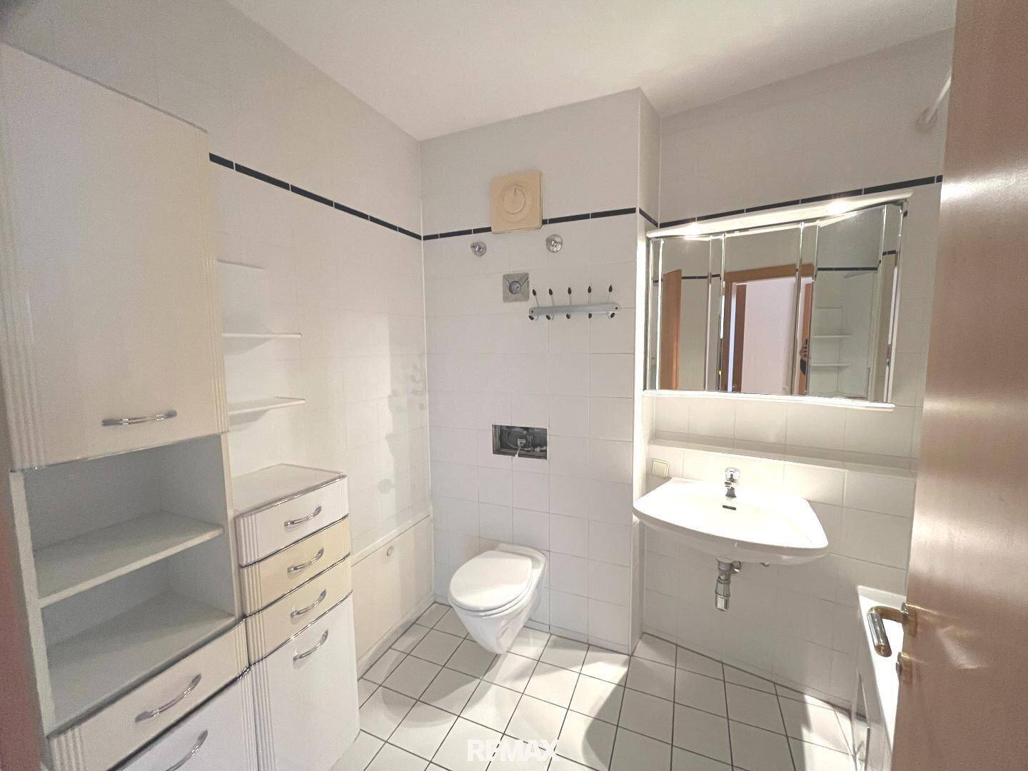Badezimmer mit weißen Fliesen, Toilette, Waschbecken und praktischen Einbauschränken.