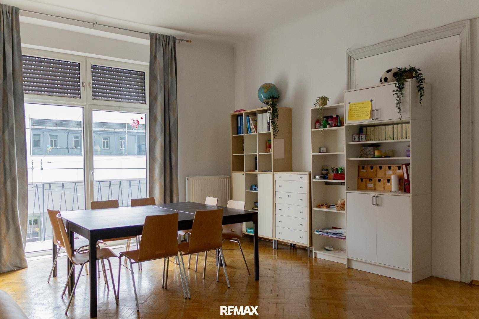 Großer Essbereich mit dunklem Tisch, Holzstühlen und Bücherregalen, mit Zugang zu einem Balkon.