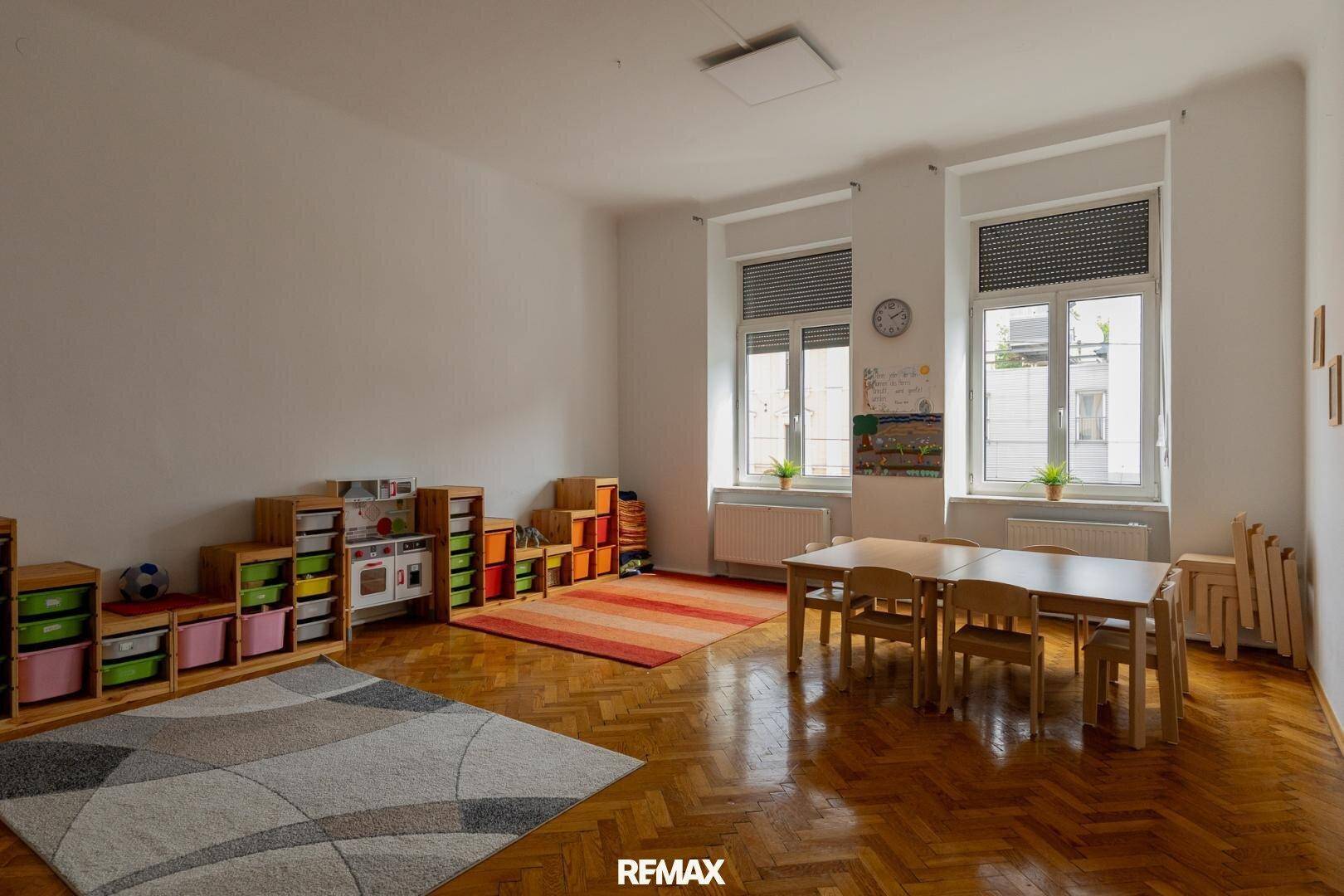 Geräumiges Kinderzimmer mit Holzparkett, Spielzeugregalen und einem kleinen Tisch mit Stühlen.