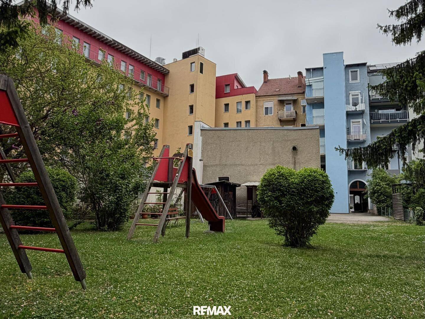 Grüner Gartenbereich mit Kinderspielplatz, umgeben von verschiedenen Wohngebäuden in unterschiedlichen Farben.