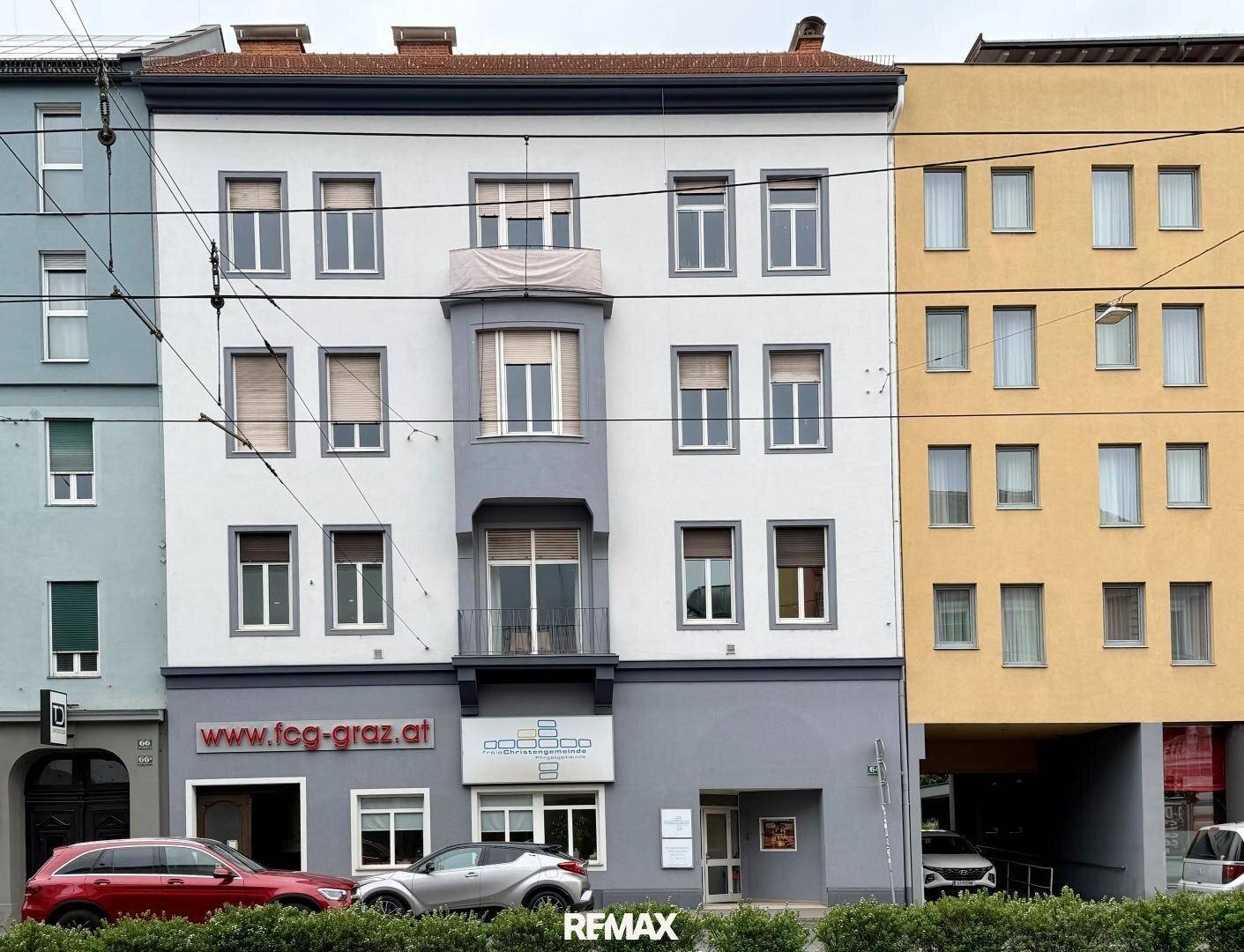 Mehrstöckiges Gebäude mit gemischter Fassade in Grau und Gelb, mit Geschäften im Erdgeschoss.