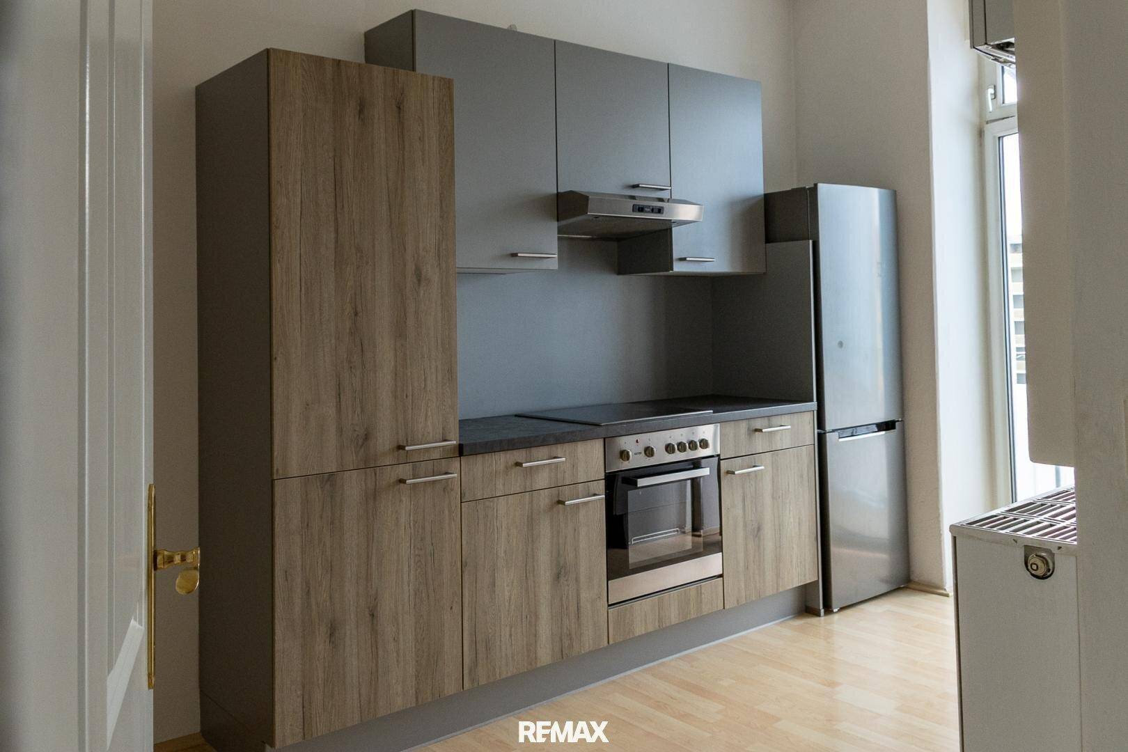 Moderne Küche mit grauen und holzfarbenen Schränken, integrierten Geräten und Kühlschrank.