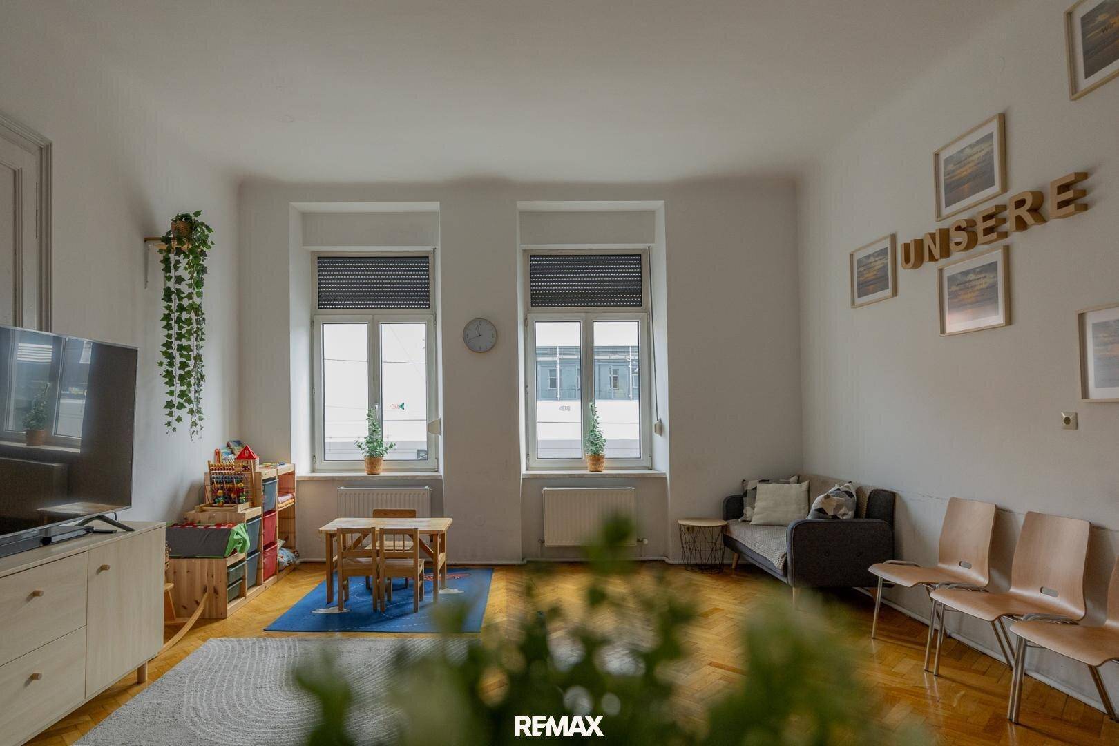 Heller Wohnraum mit Sofa, Fernseher und Kinderspielbereich, mit Blick auf die Straße.