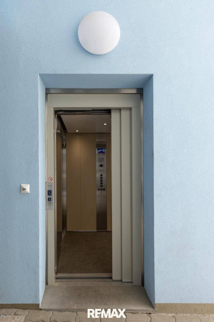 Moderner Aufzug mit geöffneten Türen in einem hellblauen Flur, bereit zur Benutzung.