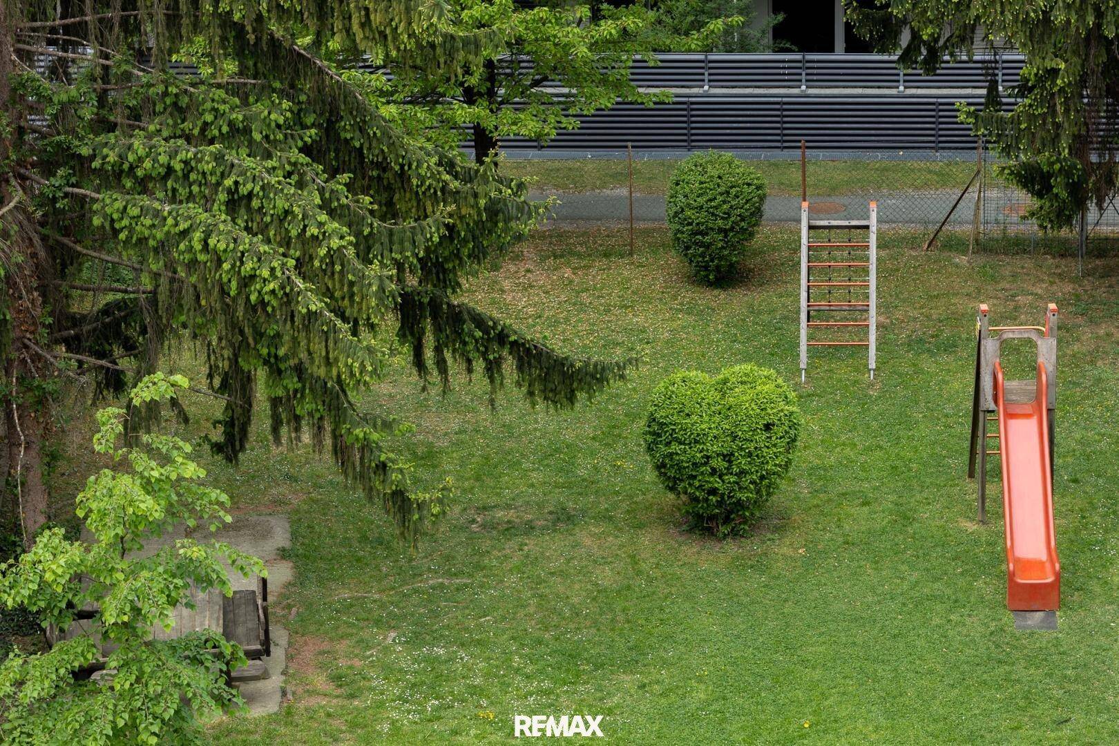Detailansicht eines grünen Gartens mit einem kleinen Kinderspielplatz, Rutsche und Klettergerüst.