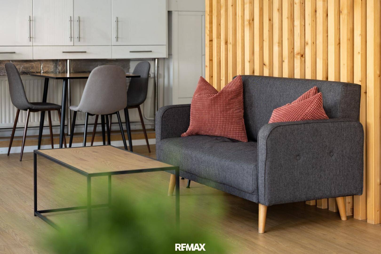 Gemütlicher Wohnbereich mit Sofa, Couchtisch und Holzwand, angrenzend an eine kleine Küche.