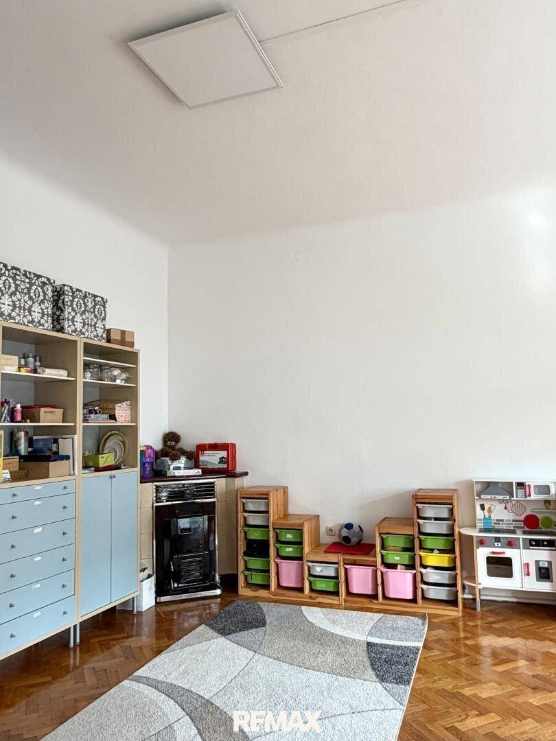 Helles Kinderzimmer mit Spielküche, Regalen und Teppich auf dem Holzparkettboden.