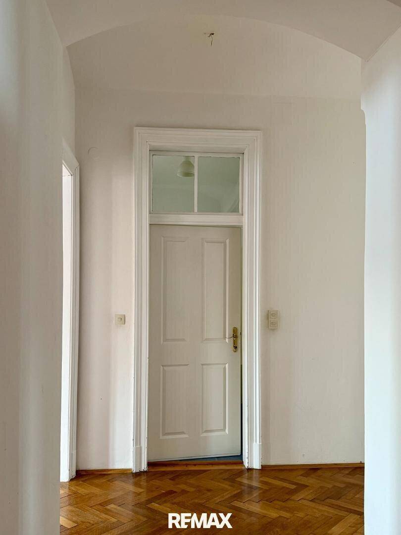 Heller Flur mit Holzboden und einer klassischen weißen Tür mit Oberlicht, die in einen Raum führt.