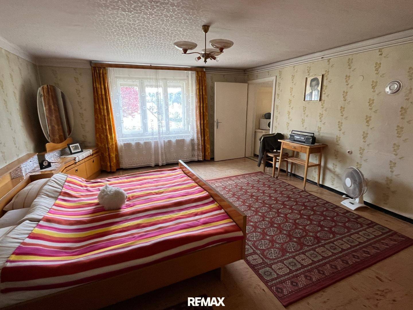 Schlafzimmer mit floraler Tapete, Holzmöbeln und farbenfroher Bettwäsche in traditionellem Stil.