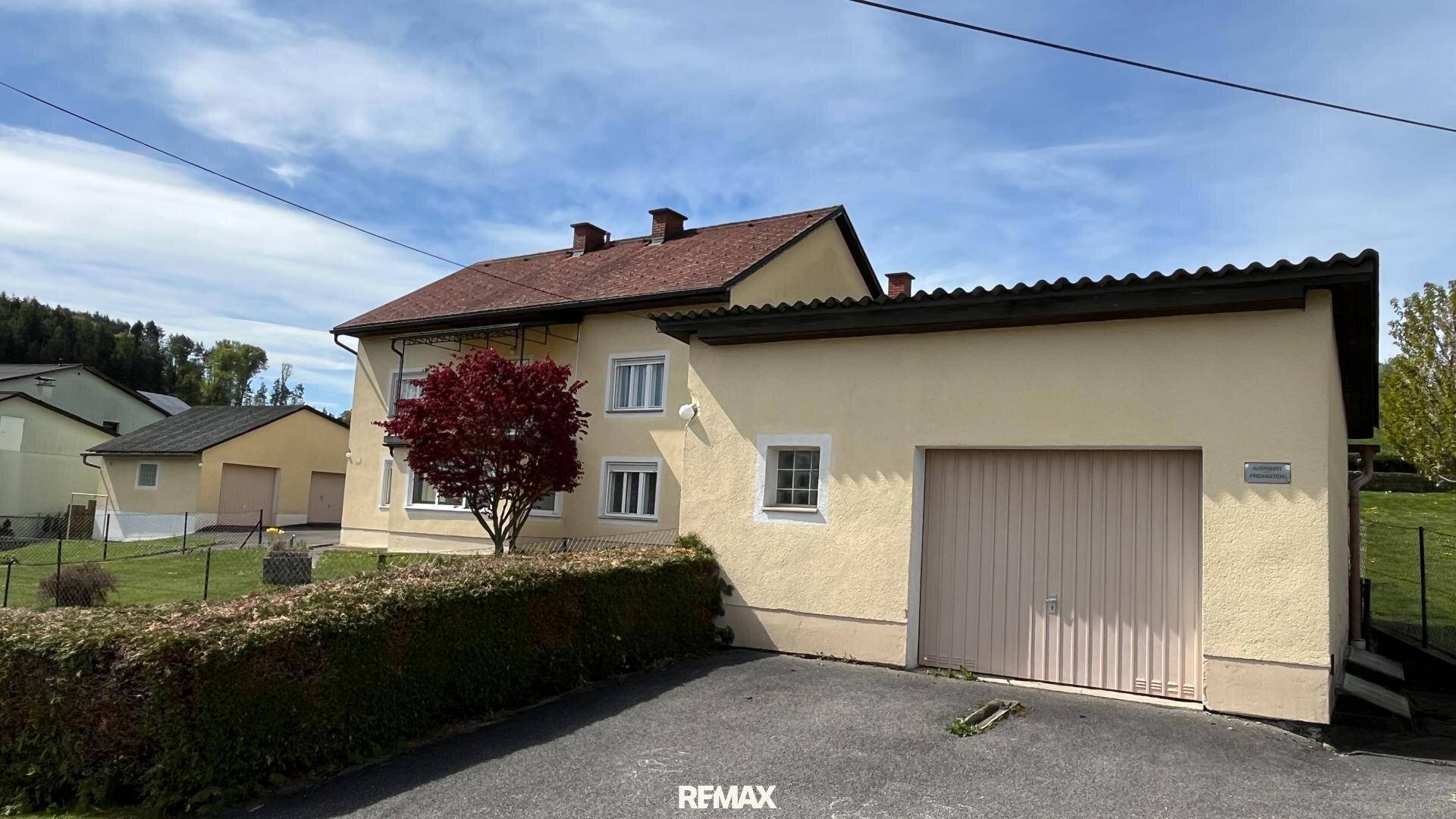 Einfamilienhaus mit angrenzender Garage und gepflegter Hecke im Vorgarten.