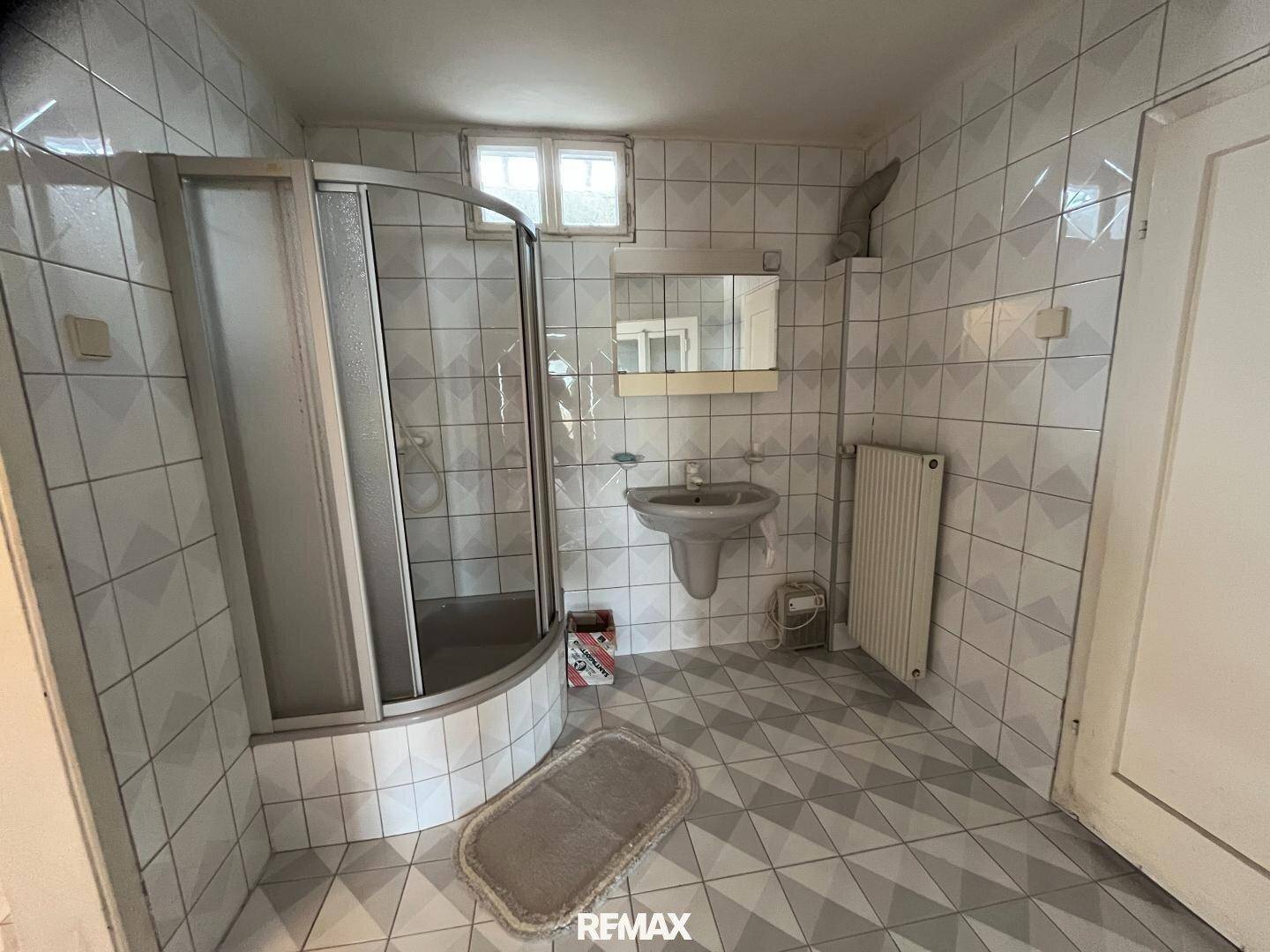 Badezimmer mit Duschkabine, Fliesenboden und kleinen Fenstern in hellem Design.
