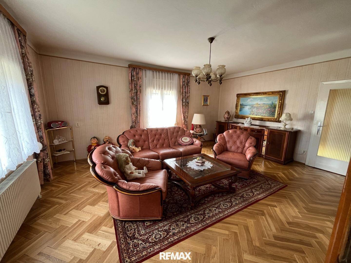 Geräumiges Wohnzimmer mit traditioneller Einrichtung, Parkettboden und floraler Tapete.