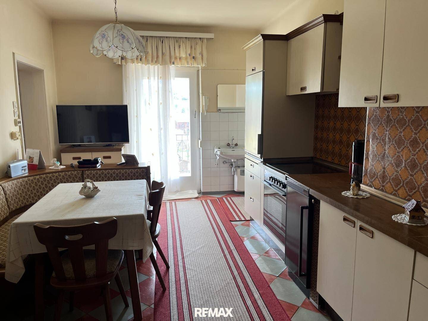 Funktionale Küche mit Essbereich, Fliesenboden und Zugang zu einem kleinen Balkon.