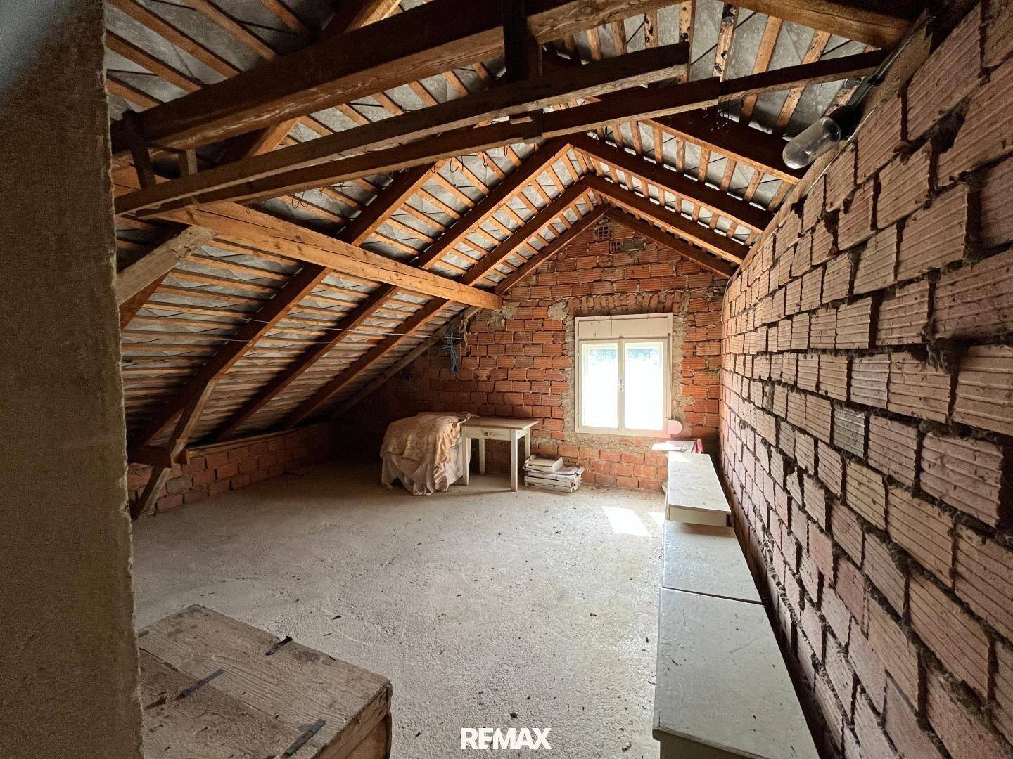 Unausgebauter Dachboden mit sichtbaren Holzbalken und Ziegelwänden, bereit für Ausbau.