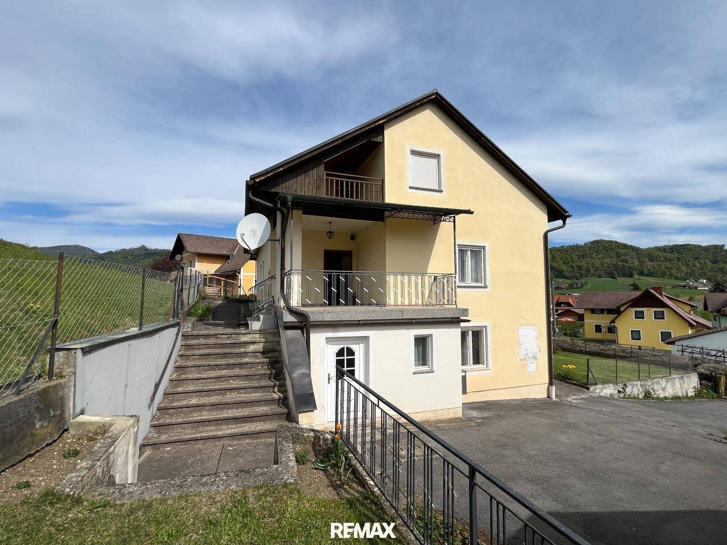 Seitenansicht des Hauses mit Außentreppe und Balkon unter blauem Himmel.