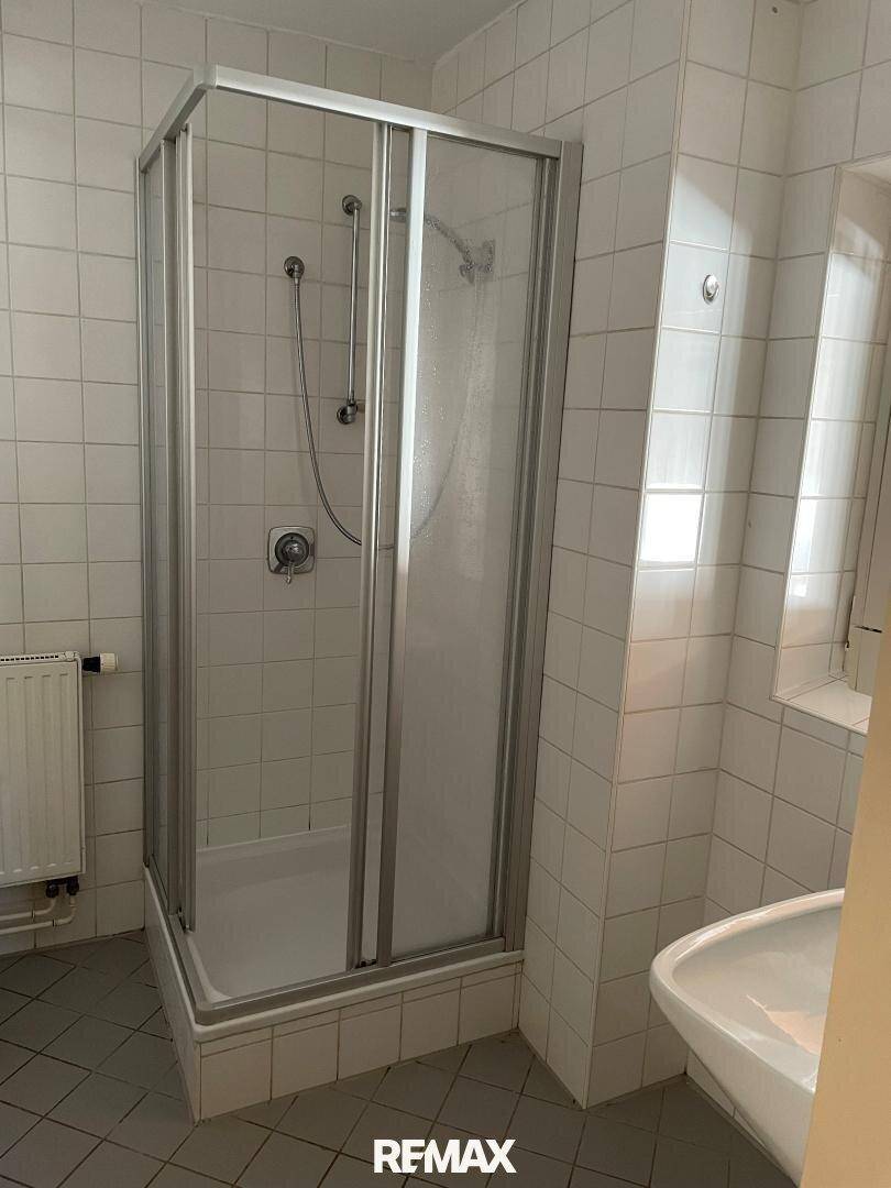 Badezimmer mit Duschkabine, Waschbecken und Fliesen an Wänden und Boden.