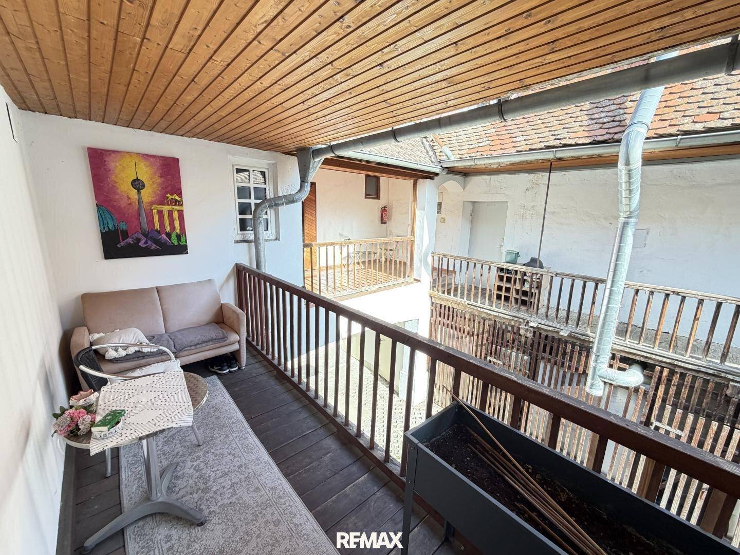 Gemütlicher Balkon mit Holzboden und -decke, möbliert und mit Blick auf den Innenhof.