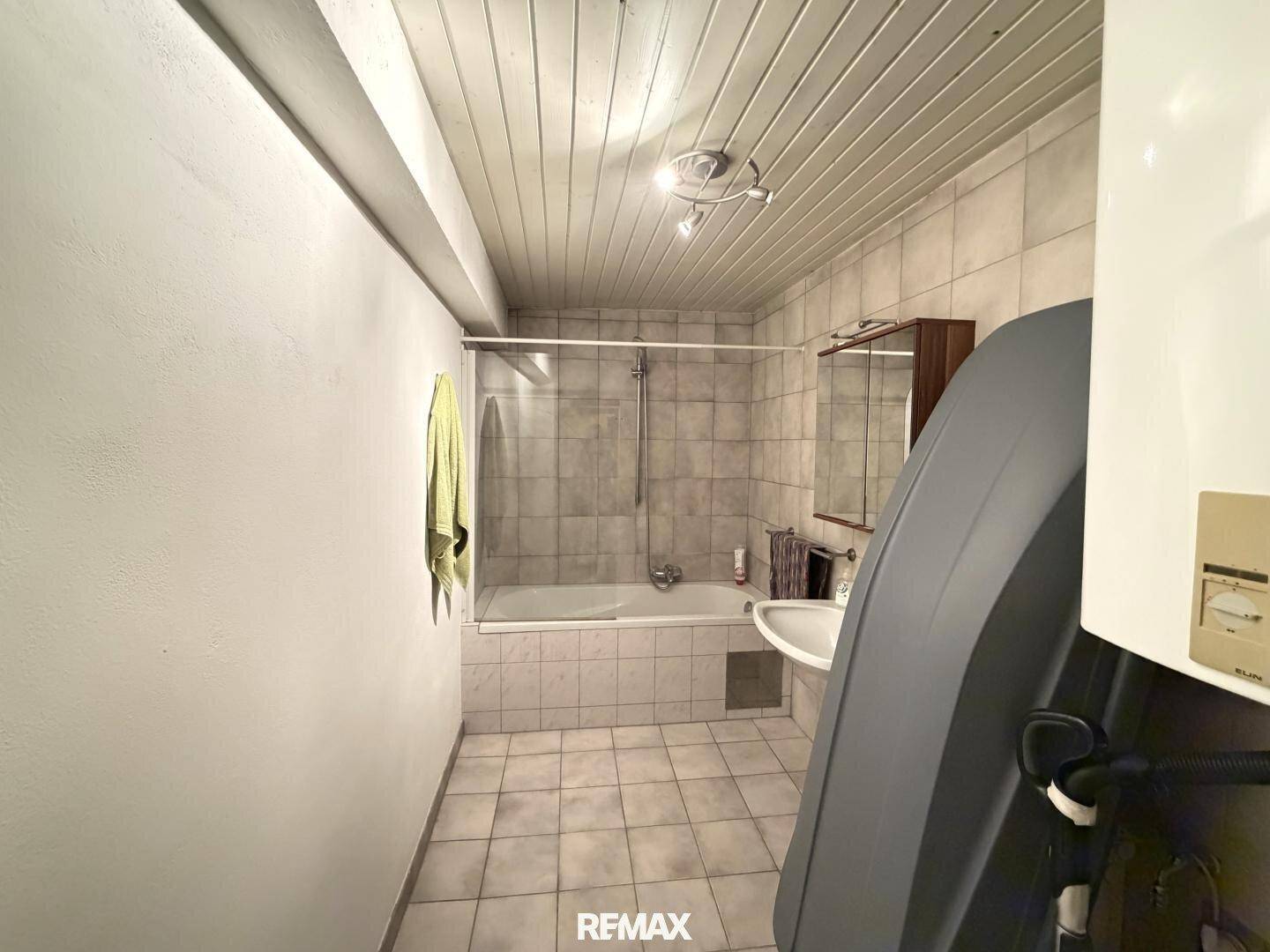 Badezimmer mit Badewanne, integrierter Dusche und Fliesen an Wänden und Boden.