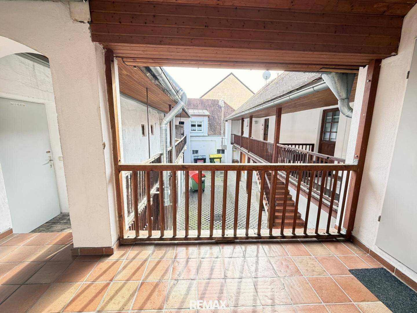 Überdachter Innenbalkon mit Holzgeländer und Blick auf den Innenhof des Gebäudes.