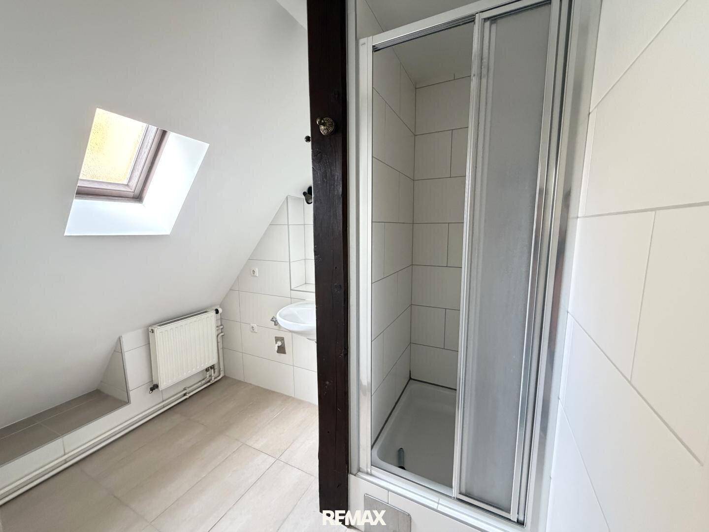 Dachgeschossbadezimmer mit Dusche, Waschbecken und Dachfenster, hell gefliest.